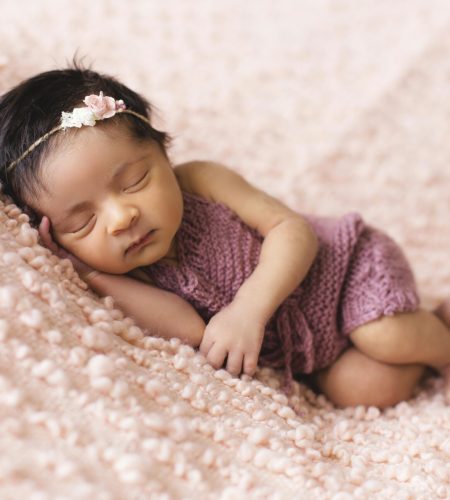 A newborn baby girl peacefully sleeps on a soft pink blanket, embodying innocence and tranquility.